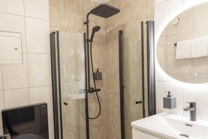 Un baño moderno con ducha envuelta en vidrio, un lavamanos blanco y un espejo.