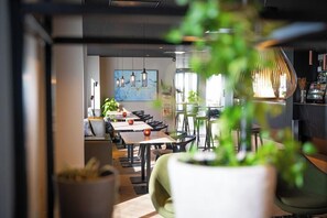 A modern interior with tables and chairs, a painting on the wall, and a potted plant in the foreground.