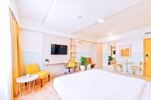 Quarto de hotel com cama, escrivaninha, duas cadeiras, televisão e mesa pequena.