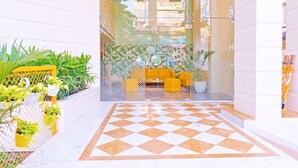 Entrada de hotel con piso a cuadros, plantas en macetas y un sofá amarillo.