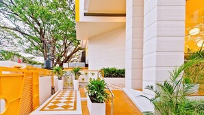 Un edificio moderno con un sendero de diseño geométrico, plantas en macetas y un árbol.