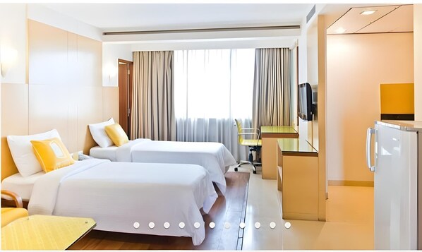 Una habitación de hotel con dos camas, un escritorio, una silla, un televisor y un refrigerador.