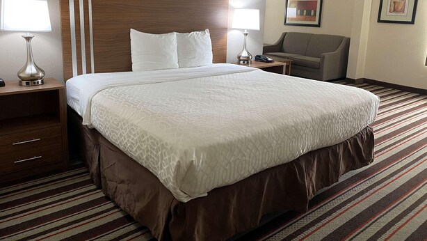 A hotel room with a large bed, two bedside tables with lamps, a chair, and a small table with a phone. - Best Western Windsor Inn & Suites (Danville)