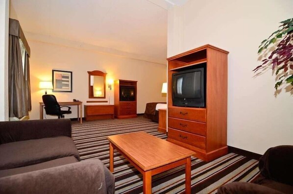 Quarto de hotel com sofá, móvel de TV de madeira, escrivaninha e cadeira.