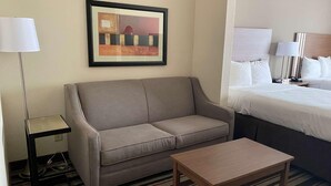 A hotel room with a sofa, a small table, a bed with white bedding, a framed picture on the wall, and a floor lamp. - Best Western Windsor Inn & Suites (Danville)