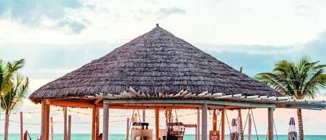 A poolside bar area with a thatched roof, lounge chairs, and a pool.