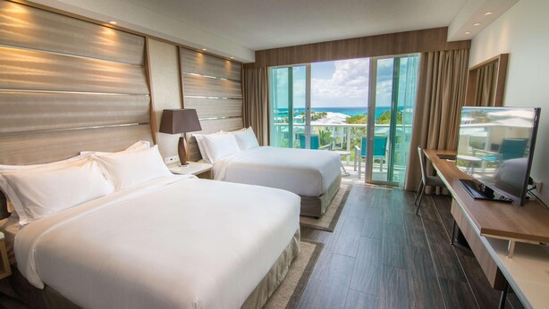 A hotel room with two beds, a TV, and a balcony with a view. - Hilton At Resorts World Bimini (Alice Town)