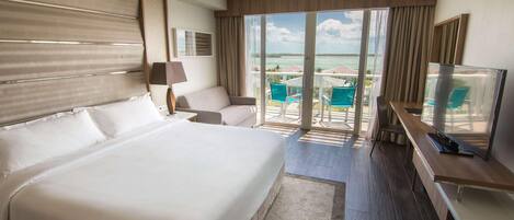 Een hotelkamer met een groot bed, een bureau, een stoel, een televisie en een balkon met uitzicht op zee.