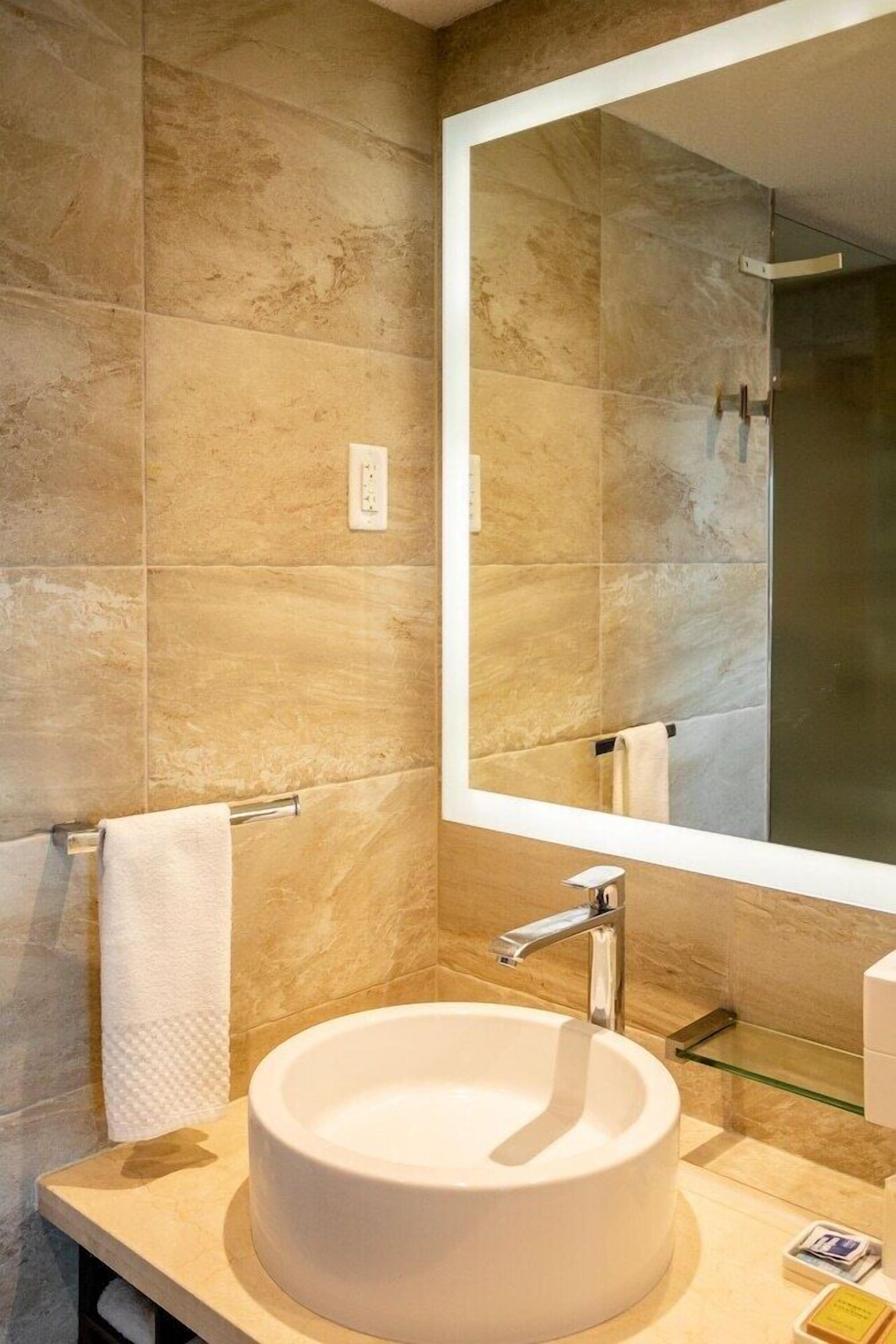 Een moderne badkamer met een grote spiegel, een rond wastafel en een glazen plank.