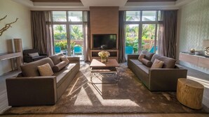A modern living room with a flat-screen TV, two sofas, a coffee table, and large windows with curtains. - Hilton At Resorts World Bimini (Alice Town)