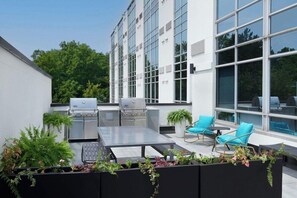 En tagterrasse med grill, siddepladser og krukker med planter.