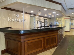 A reception desk with a 'RAMADA' sign, framed artwork, and a 'RESTROOMS' sign in the background. - Ramada By Wyndham Niagara Falls By the River (Niagara Falls)