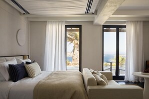 A modern hotel room with a bed, a sofa, and a view of the sea. - Anandes Hotel - Adults Only (Mykonos)