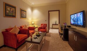 A hotel room with a red sofa, a glass coffee table, a TV, and a dining area with a chair and table. - Corp Al Khobar Corniche Hotel (Al Khobar)