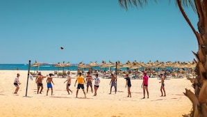 A beach volleyball game on a sandy beach with umbrellas and lounge chairs in the background. - Occidental Marco Polo (Hammamet)
