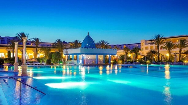 A large swimming pool with a gazebo in the center, surrounded by palm trees and hotel buildings. - Occidental Marco Polo (Hammamet)