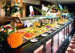 Un bufé con diversos alimentos y un chef al fondo.