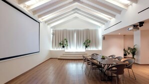 A conference room with a large screen, wooden flooring, a high ceiling with exposed beams, a window with curtains, and several chairs around a table. - Aulus Chania Resort, Curio Collection by Hilton (Chania)