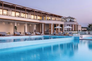 Ein modernes Hotel mit einem großen Außenpool, Liegestühlen und einem Balkon mit Sitzgelegenheit im zweiten Stock.
