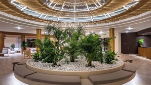 A modern lobby with a circular seating area, a central plant arrangement, and a unique ceiling design. - Aulus Chania Resort, Curio Collection by Hilton (Chania)