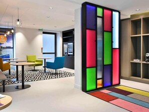 A modern hotel lobby with a geometric patterned floor, a seating area with tables and chairs, and a colorful partition wall. - Mercure Boulevard Magenta (Paris)
