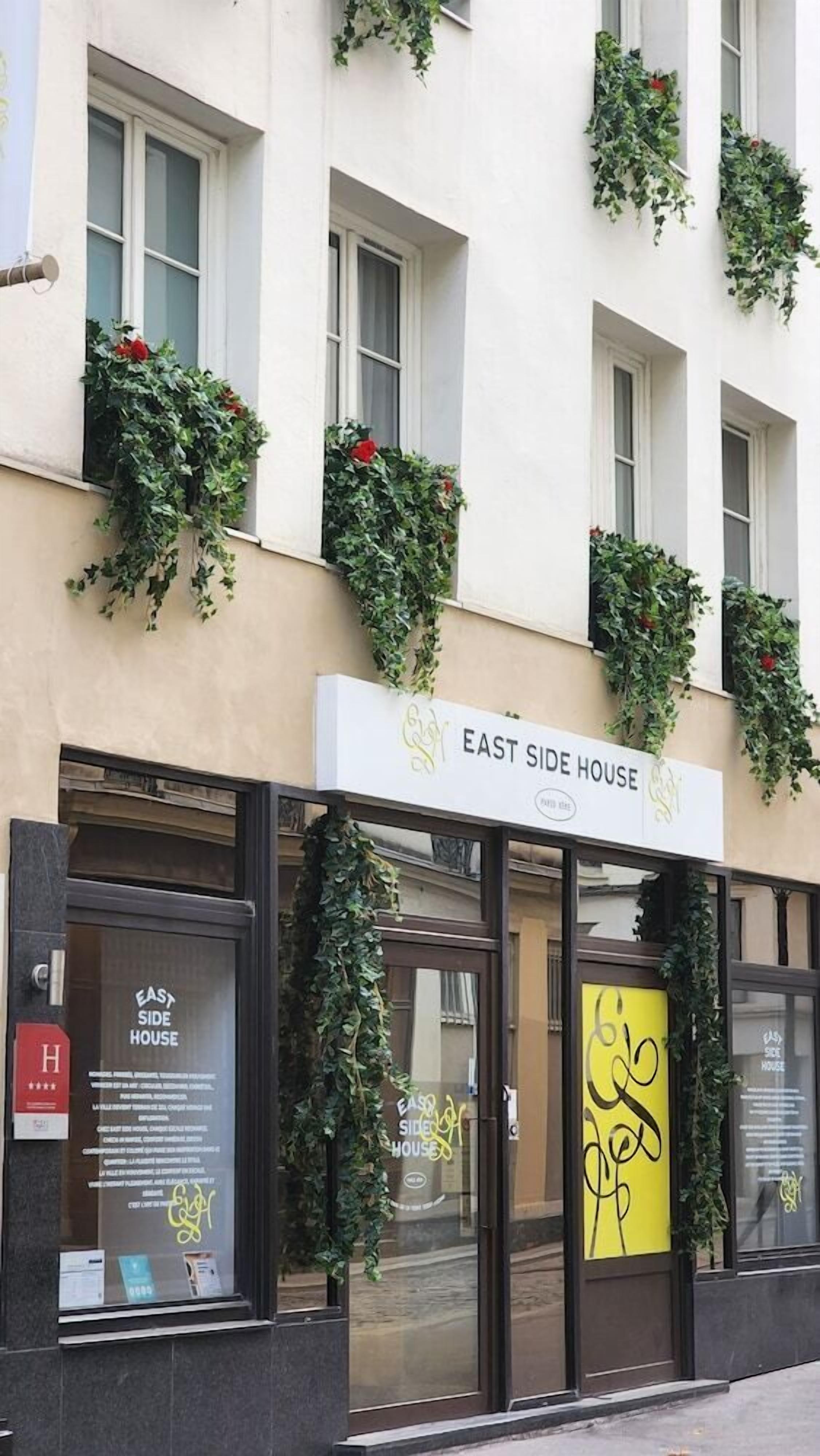 En byggnad med en skylt som visar texten ”EAST SIDE HOUSE” och fönster som är dekorerade med grönska.