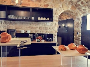 A rustic kitchen with stone walls, wooden shelves, and a breakfast setup with croissants. - Mercure Boulevard Magenta (Paris)