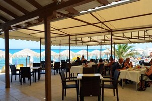 Un espacio exterior para comer con mesas y sillas, techo cubierto y vista al mar.