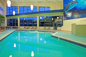 An indoor swimming pool with clear blue water, surrounded by lounge chairs and umbrellas, and a mural of a dolphin on the wall. - Wyndham Flint Mi/grand Blanc/bishop Airport/conference Ctr (Flint)