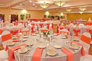 A banquet hall with round tables set for a formal event, featuring white tablecloths and orange sashes. - Wyndham Flint Mi/grand Blanc/bishop Airport/conference Ctr (Flint)