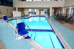 An indoor swimming pool with a blue tiled floor, a lifeguard chair, and lounge chairs. - Wyndham Flint Mi/grand Blanc/bishop Airport/conference Ctr (Flint)
