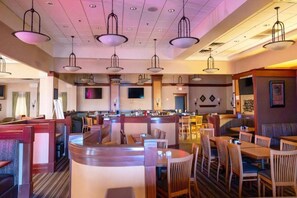 A restaurant with booths, tables, and hanging pendant lights. - Wyndham Flint Mi/grand Blanc/bishop Airport/conference Ctr (Flint)