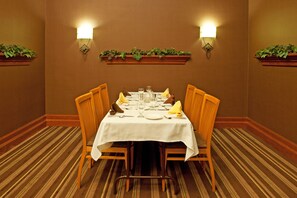 A dining room with a table set for four, surrounded by chairs, with wall-mounted lights and greenery. - Wyndham Flint Mi/grand Blanc/bishop Airport/conference Ctr (Flint)