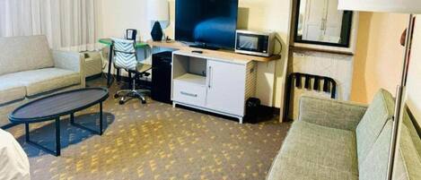 A hotel room with a sofa, a small table, a TV, a microwave, and a desk with a chair.