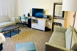 A hotel room with a sofa, a small table, a TV, a microwave, and a desk with a chair. - Wyndham Flint Mi/grand Blanc/bishop Airport/conference Ctr (Flint)