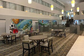 A spacious lobby with multiple seating areas, a staircase, and a mural on the wall. - Wyndham Flint Mi/grand Blanc/bishop Airport/conference Ctr (Flint)