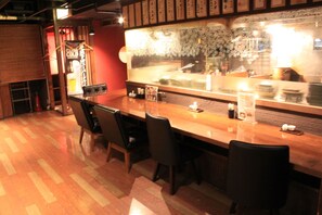 A restaurant interior with a wooden bar, black chairs, and a counter with various items. - Ascent Inn Sapporo (Sapporo)