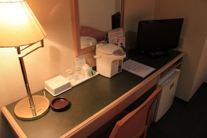Ein Schreibtisch im Hotelzimmer mit einer Lampe, einer Kaffeemaschine, einem Fernseher und einem kleinen Kühlschrank.