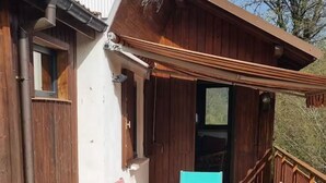 Puisesta laudasta rakennettu terassi, jossa on pöytä ja tuolit, puinen aita ja rakennus, jonka katto on kalteva.