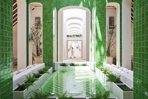 A corridor with a central water feature, white seating areas, and green tiled walls.