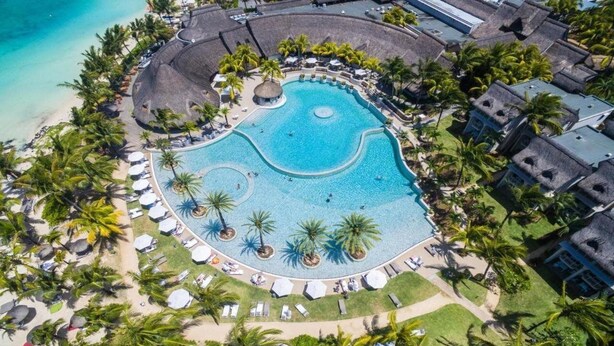 An aerial view of a resort with a large circular pool surrounded by palm trees and lounge chairs. - LUX Belle Mare Resort and Villas (Belle Mare)