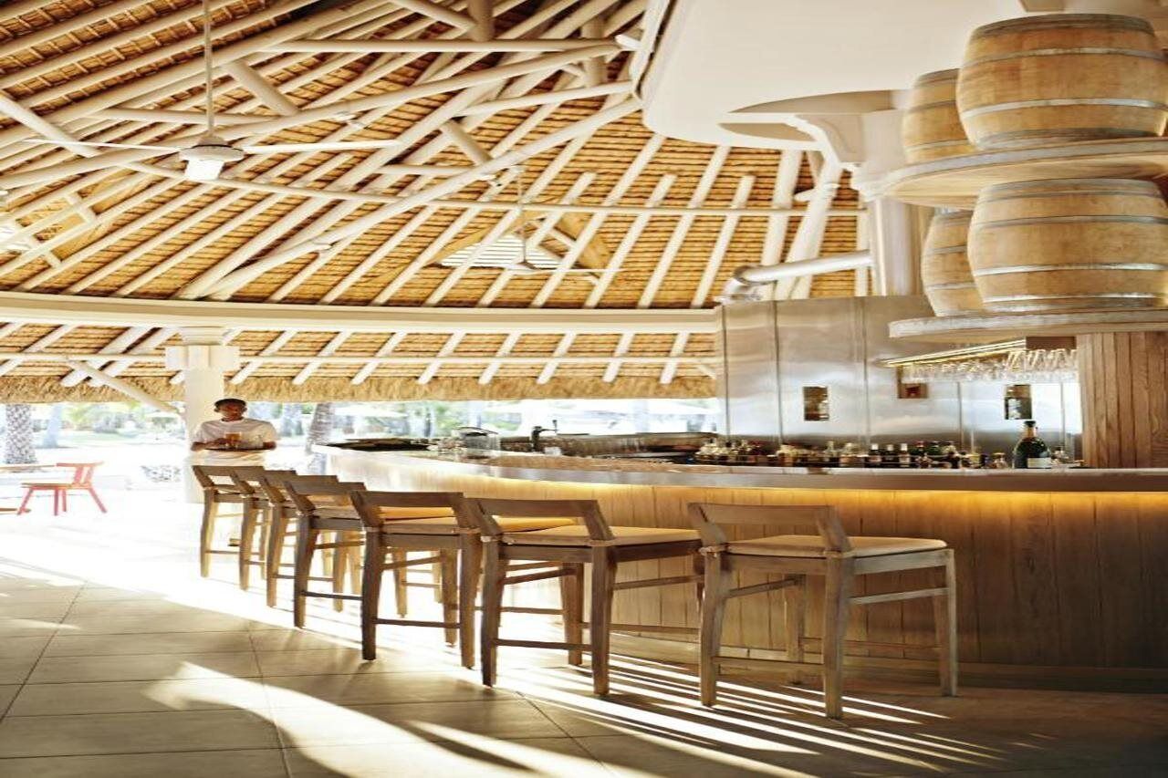 Una zona de bar con sillas de madera, una barra y un techo con diseño de paja.