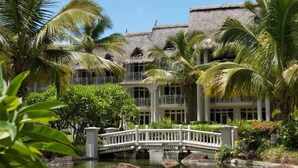 A resort with a thatched-roof building, palm trees, a bridge, and a water feature. - LUX Belle Mare Resort and Villas (Belle Mare)