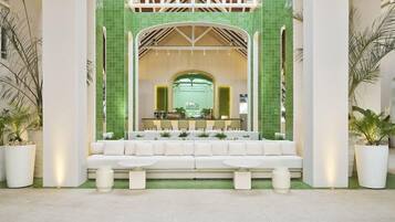 Un vestíbulo con un sofá blanco, dos mesas redondas y una zona de recepción con un muro de azulejos verdes.