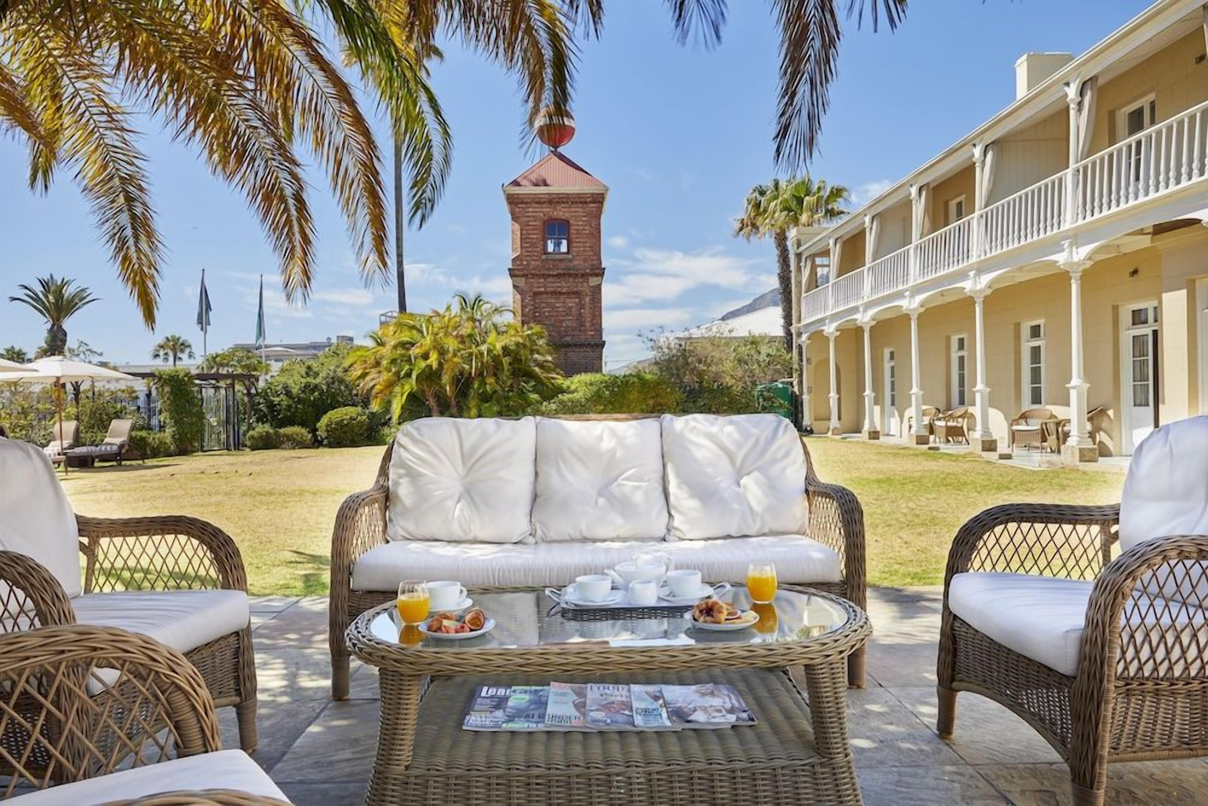 A patio area with wicker furniture, a dining table with breakfast items, and a building with a tower in the background.
