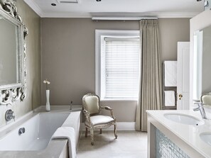 A bathroom with a bathtub, a sink, a chair, and a window with curtains. - Dock House Boutique Hotel (Cape Town)