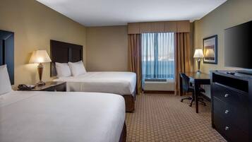 A hotel room with two beds, a desk, a chair, a television, and a window with curtains.