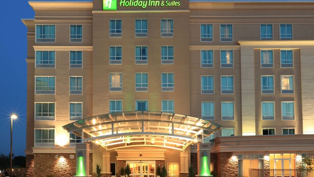 Edificio de Holiday Inn & Suites con entrada de vidrio, múltiples ventanas y fachada de piedra.