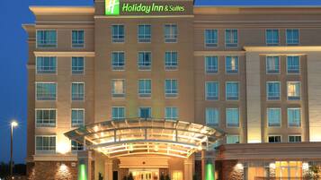 A Holiday Inn & Suites building with a glass entrance, multiple windows, and a stone facade.