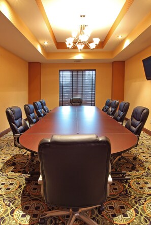 Un salón de conferencias con una larga mesa, sillas de cuero negro, alfombra estampada y un candelabro.